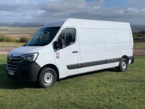 Camionnette blanche garée sur pelouse avec paysage de campagne en arrière-plan.