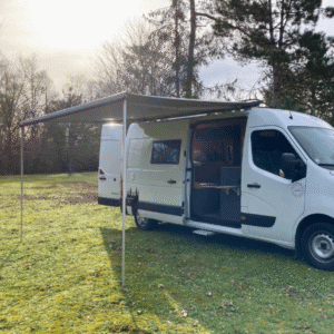 Camionnette aménagée avec auvent sur pelouse, porte ouverte, entourée d'arbres.