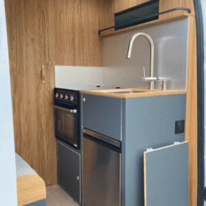 Cuisine moderne et compacte avec évier, four, plaque, frigo, bois et métal.