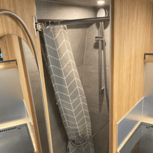 Douche moderne avec parois bois clair, carrelage gris, pommeau et rideau gris géométrique.
