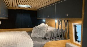 Intérieur de chambre compacte avec lit double, murs et plafond en bois, placards sombres.