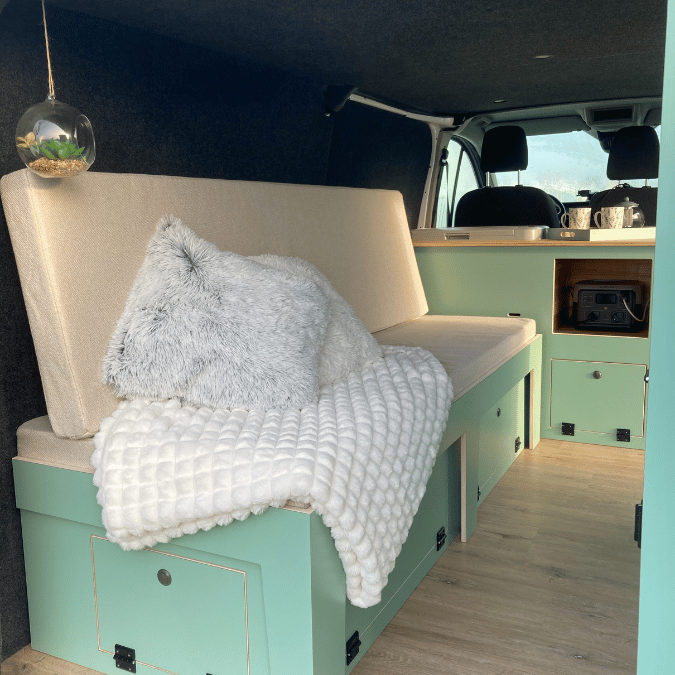 Aménagement Cocooning de Véhicule Aménagement intérieur d'un véhicule avec canapé beige, coussins, couverture et déco suspendue.