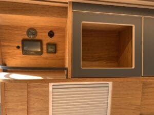 Aménagement intérieur en bois avec commandes, rangement ouvert et volets roulants.