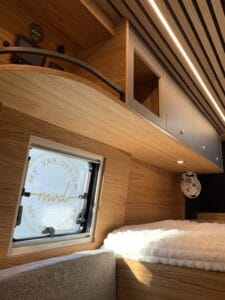 Aménagement intérieur de fourgon avec placards en bois, éclairage intégré et fenêtre logo.