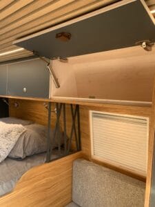 Chambre avec lits superposés, placards en bois clair, détails métalliques, store blanc.