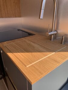 Plan de travail en bois clair, robinet inox, plaque de cuisson à gauche.