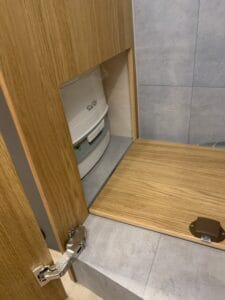 Plomberie intégrée derrière une porte de placard en bois ouverte avec surface carrelée.