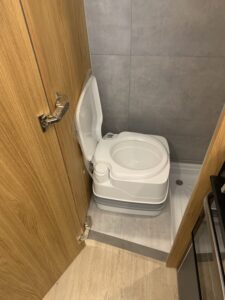 Toilette portable blanche dans un petit espace avec panneaux bois et carreaux gris.
