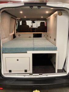 Aménagement intérieur d'un fourgon avec lit pliable et rangements visibles depuis l'arrière.