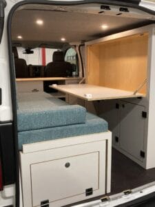 Aménagement intérieur de van avec sièges rembourrés, bureau rabattable et rangements intégrés.