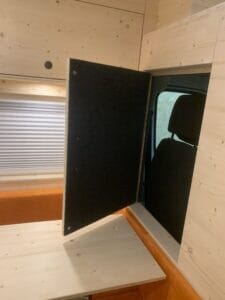 Intérieur bois clair de véhicule avec table pliante et panneau isolant ouvert sur banquette orange.