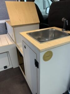 Kitchenette intégrée avec évier inox, robinet moderne, espace rangement et finitions bois clair.