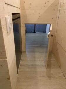 Petite porte en bois ouverte, vue sur sol et murs en bois, pièce en arrière-plan.