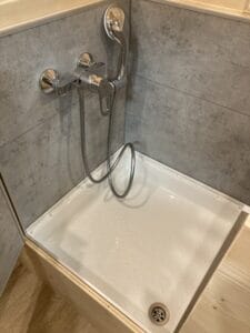 Receveur de douche carré, pommeau chromé mural, carrelage gris, finition bois clair.