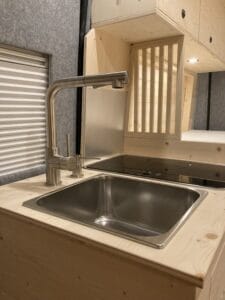 Évier en acier inoxydable sur plan de travail en bois clair avec robinet moderne, arrière cloison bois.