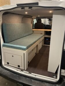 Aménagement de van avec canapé convertible en lit, rangements, et éclairage intégré.