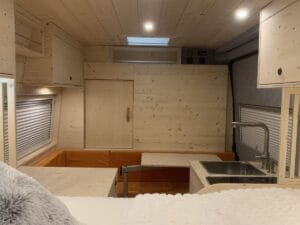 Espace intérieur de véhicule en bois clair avec cuisine, salon coussins orange, puits de lumière.