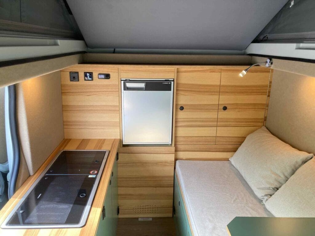Intérieur d'un espace compact avec lit, plan de cuisson, réfrigérateur et éclairage dirigé.