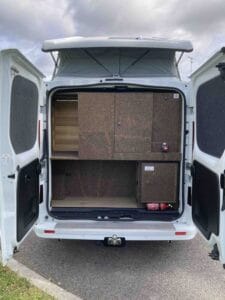Fourgon aménagé avec portes arrière ouvertes, espace de rangement, placards, étagère, extincteur.